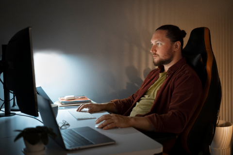 Man sitting at his home office in front of a desktop computer, utilizing UsenetServer's Global Search Tool for comprehensive Usenet article searches.