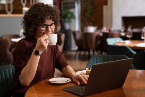 Woman at a coffee shop using a laptop to access UsenetServer's Global Search Tool, enjoying an easy and secure Usenet browsing experience.